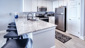 Una cocina con gabinetes blancos, un refrigerador de acero inoxidable, un microondas y una estufa.