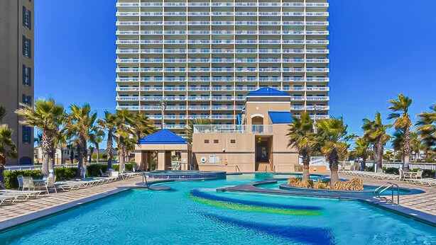 Ein Hotel mit großem Pool, Palmen und einem Hochhaus im Hintergrund.