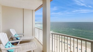 Ein Balkon mit zwei weißen Lounge-Stühlen und Blick auf Strand und Meer.