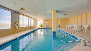 Ein Hallenbad mit klarem, blauem Wasser, einem Rettungsschwimmerstuhl und weißen Liegestühlen rund um den Pool.