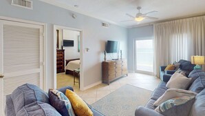 Ein Wohnzimmer mit einer Couch, einem Fernseher, einem Schminktisch und einem Deckenventilator.