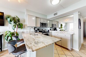 A modern kitchen with white cabinets, a marble countertop, and a large island. - 505A - Waterview condo w/ open layout, W/D, & AC - hot tub, pool, & tennis court (Gulf Shores)