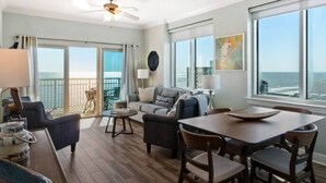 A spacious living area with a balcony, a dining table, and a sofa. - Gorgeous Gulf view condo with indoor,outdoor pools, hot tubs, gym, & balconies (Gulf Shores)