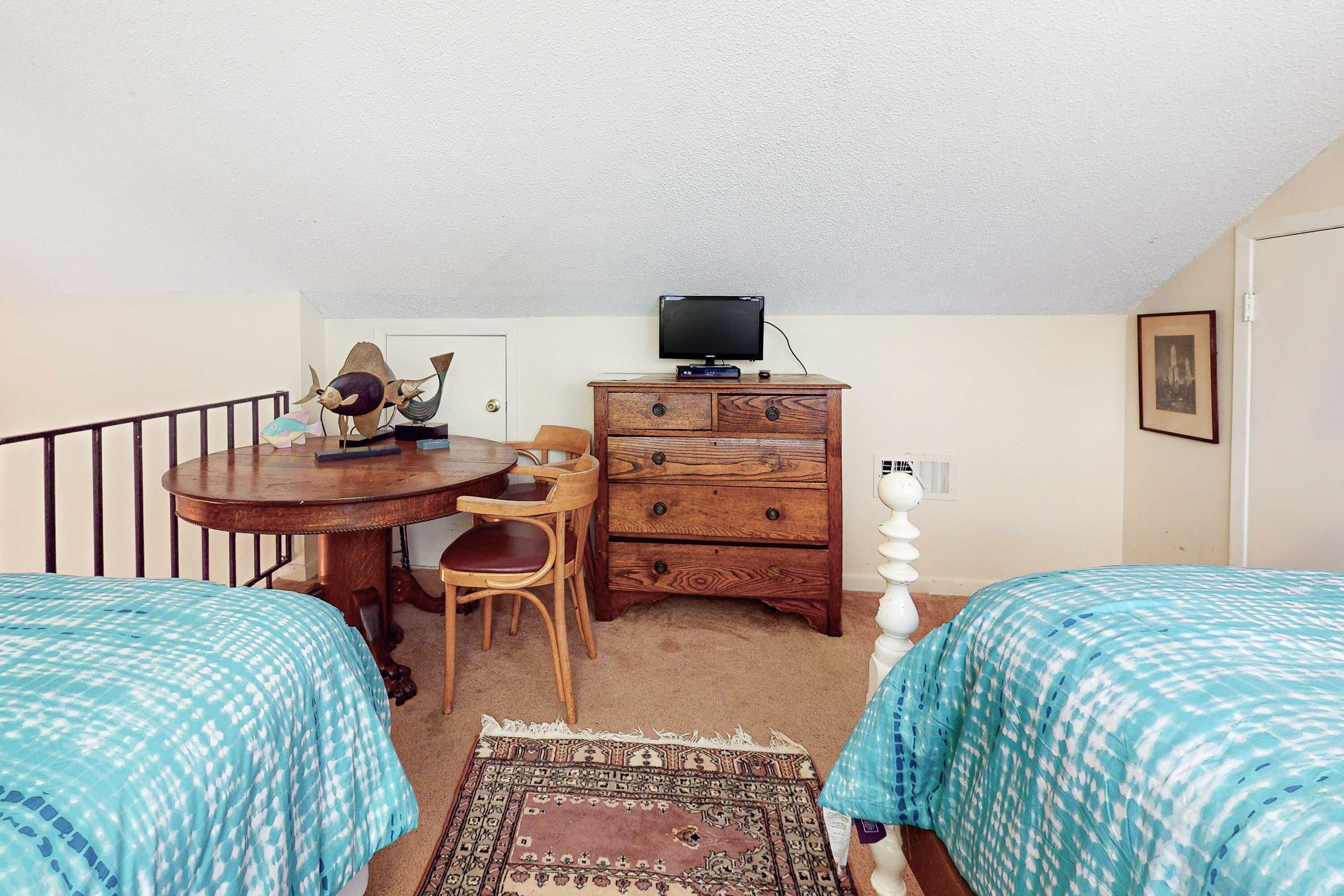 Ein Schlafzimmer mit zwei Betten, einem Schreibtisch mit Stuhl, einer Kommode, einem Fernseher und einem gemusterten Teppich.