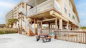 A multi-story hotel with outdoor balconies, a pool, and a wooden deck with picnic tables. - Beachfront condo with outdoor pool, beach views, washer/dryer, beach access (Gulf Shores)