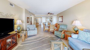 A living room with a television, two sofas, a dining table, and chairs. - Beach/Gulf-front condo with water views, on-site pool, & private balcony (Gulf Shores)