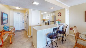 A kitchen with a central island, bar stools, and a dining table with chairs. - Beach/Gulf-front condo with water views, on-site pool, & private balcony (Gulf Shores)