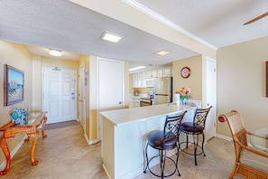 A kitchen with a central island, bar stools, and a dining table with chairs. - Beach/Gulf-front condo with water views, on-site pool, & private balcony (Gulf Shores)
