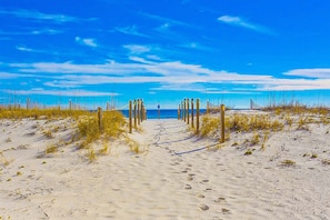 A sandy beach path leading to the sea with wooden posts, clear sky, and footprints. - Beach-front condo with water views, on-site pool, & private balcony (Gulf Shores)
