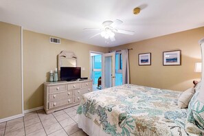 A bedroom with a bed, dresser, television, ceiling fan, and a door leading to a balcony. - Beachfront retreat with outdoor pool, gulf views, & W/D - perfect for long stays (Gulf Shores)
