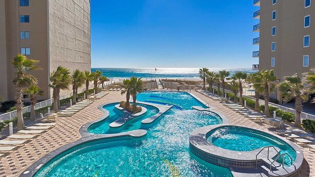 A hotel pool area with multiple swimming pools, palm trees, and a view of the ocean. - Gulf view condo with 2 pools, lazy river, hot tub, sauna, gym & beach access (Gulf Shores)