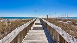 A wooden boardwalk leading to a beach with an American flag. - Gulf view condo with 2 pools, lazy river, hot tub, sauna, gym & beach access (Gulf Shores)