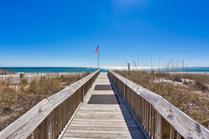 A wooden boardwalk leading to a beach with an American flag. - Gulf view condo with 2 pools, lazy river, hot tub, sauna, gym & beach access (Gulf Shores)