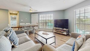 Uma sala de estar com sofá, mesa de centro, televisão e área de refeições.