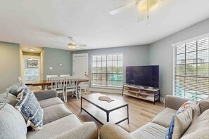 A living room with a sofa, coffee table, TV, and dining area. - 2-story home near the beach with deck, outdoor shower, W&Ds, 2 kitchens (Gulf Shores)