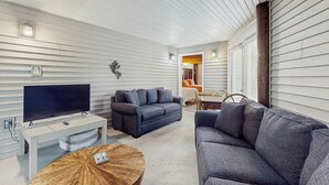 Sala de estar com televisão de tela plana, dois sofás, uma mesa de centro e um espaço de jantar com mesa e cadeiras.