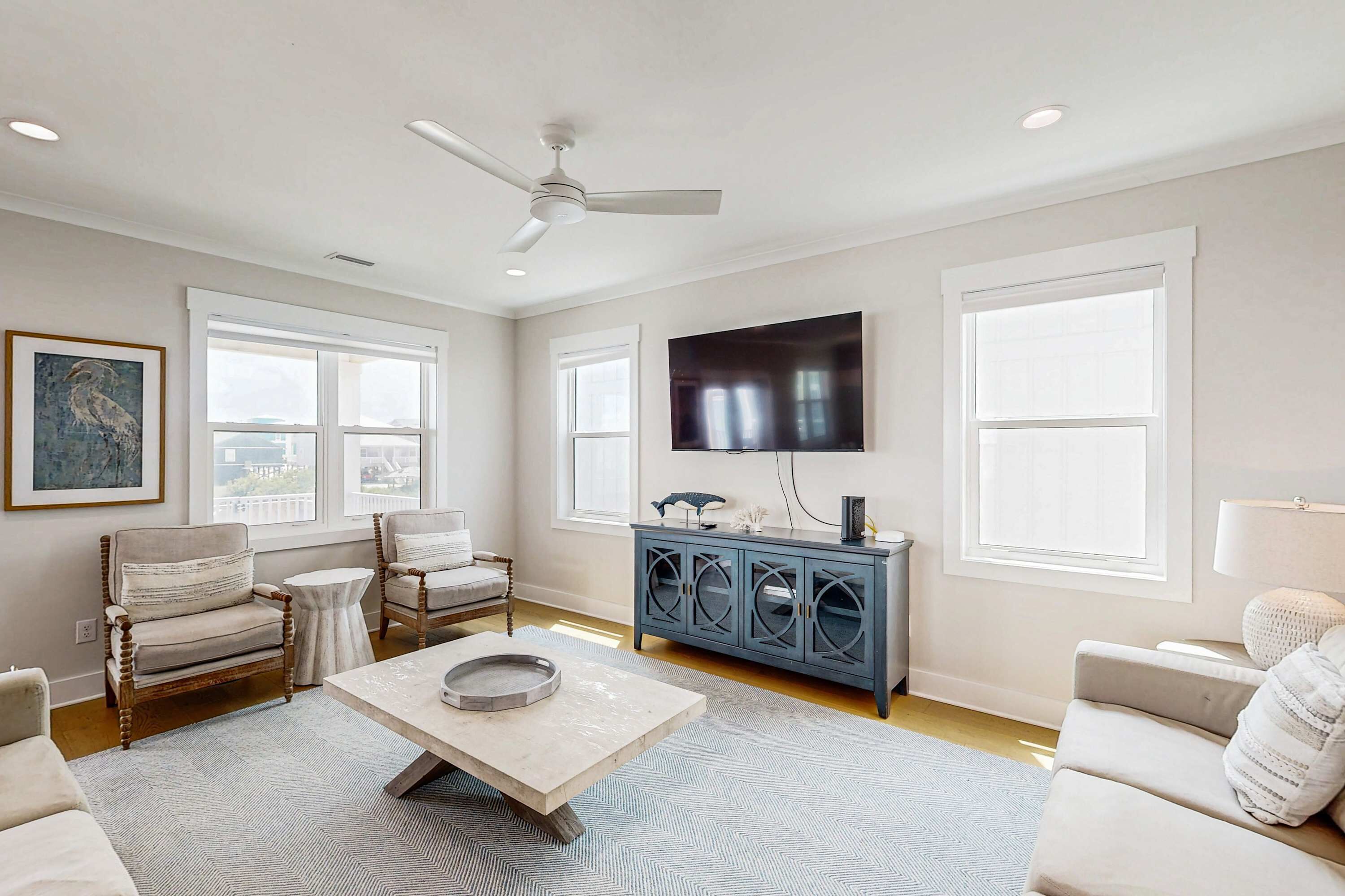 A living room with a ceiling fan, a TV mounted on the wall, and a large window.
