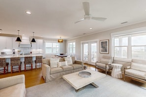 A spacious living area with a sofa, chairs, a coffee table, and a kitchen in the background. - Sprawling retreat with an enclosed pool, large balcony, outdoor shower, & W&D (Gulf Shores)