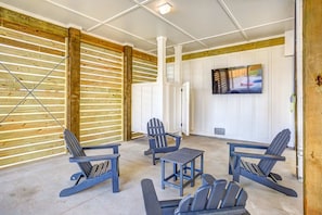 A room with wooden slats on the walls, a television mounted on the wall, and several Adirondack chairs and a small table. - Sprawling retreat with an enclosed pool, large balcony, outdoor shower, & W&D (Gulf Shores)
