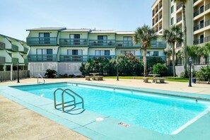 A swimming pool with a metal ladder, surrounded by a fence, with a multi-story building in the background. - Renovated condo by the beach with pool access & private balconies (Gulf Shores)