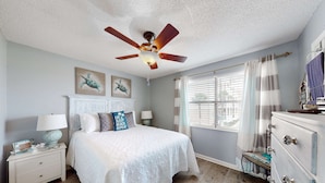 A bedroom with a bed, nightstands, a dresser, a ceiling fan, and artwork on the wall. - Renovated condo by the beach with pool access & private balconies (Gulf Shores)