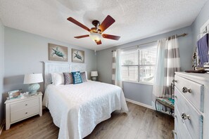 A bedroom with a bed, nightstands, a dresser, a ceiling fan, and artwork on the wall. - Renovated condo by the beach with pool access & private balconies (Gulf Shores)