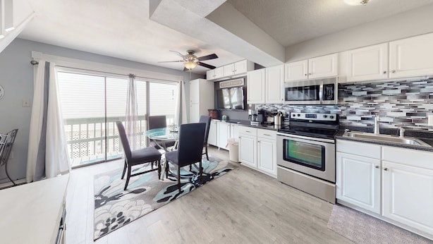A modern kitchen with white cabinets, a microwave, an oven, and a dining area with a table and chairs. - Renovated condo by the beach with pool access & private balconies (Gulf Shores)