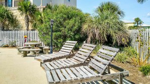 Outdoor lounge chairs, a concrete patio, and a wooden fence with greenery. - Renovated condo by the beach with pool access & private balconies (Gulf Shores)