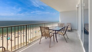 Een balkon met een tafel en stoelen, met uitzicht op een strand met parasols en mensen.