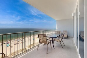 Ein Balkon mit Tisch und Stühlen, der einen Blick auf einen Strand mit Sonnenschirmen und Menschen bietet.