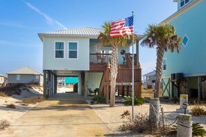 A two-story beach house with a balcony, a flag, and a sign that reads 'BEACH HAPPY.' - Pristine beach home with gulf view, covered patio, and AC (Gulf Shores)