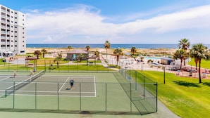 Ein Tennisplatz mit Blick auf den Strand und den Ozean, umgeben von Palmen und einem Gebäude.