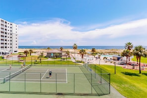 Ein Tennisplatz mit Blick auf den Strand und den Ozean, umgeben von Palmen und einem Gebäude.