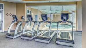 Vier loopbanden in een sportschool, met een zwembad zichtbaar door de glazen deuren.