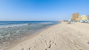 Een strand met voetafdrukken, een heldere lucht en gebouwen op de achtergrond.