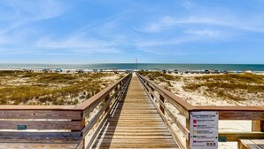 Pasarela de madera que lleva a una playa, con un letrero de advertencia.