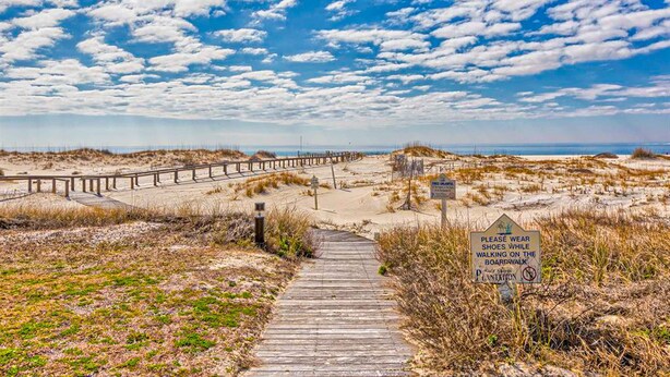 Une promenade en bois mène à une plage, et un panneau invite les visiteurs à porter des chaussures.