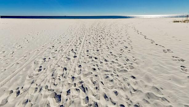 Une plage de sable où l’on peut voir des empreintes de pas qui mènent vers l’eau.