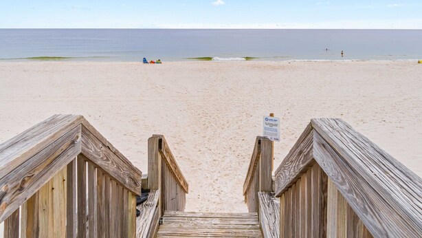 Een houten vogelzangpad leidt naar een zandstrand onder een heldere lucht.