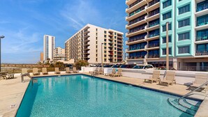 A swimming pool with lounge chairs, a lifeguard stand, and a view of high-rise buildings. - Gulf front condo with stunning Gulf views, outdoor pool & beach access (Gulf Shores)