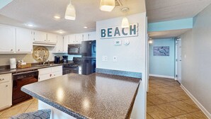 A kitchen with granite countertops, white cabinets, and a 'BEACH' sign on the wall. - Gulf front condo with stunning Gulf views, outdoor pool & beach access (Gulf Shores)