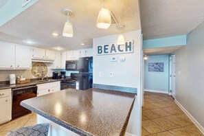 A kitchen with granite countertops, white cabinets, and a 'BEACH' sign on the wall. - Gulf front condo with stunning Gulf views, outdoor pool & beach access (Gulf Shores)