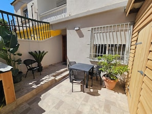 Eine kleine Terrasse mit Tisch und Stühlen, umgeben von Kübelpflanzen und einem Holzzaun.
