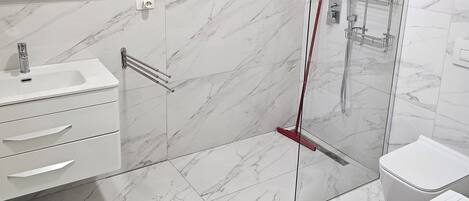A modern bathroom with a glass shower enclosure, white marble tiles, a white sink with a mirror, and a white toilet.