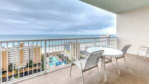 A balcony with a white table and chairs, overlooking a beach and pool area. - Corner condo with Gulf lagoon views, beach access & pools lazy river (Gulf Shores)