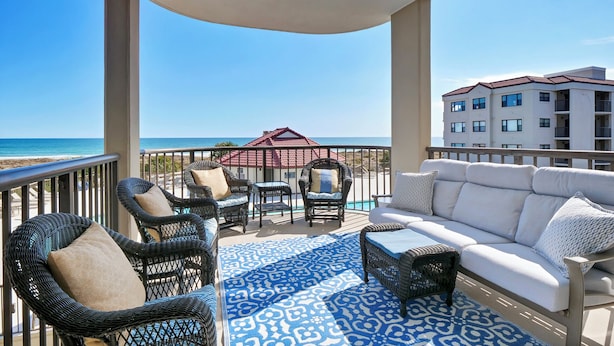 A balcony with wicker furniture, a white sofa, and a patterned rug. - 3BR/3BA Dune Ridge Condo with Elevator, Pool & Ocean Views (Wrightsville Beach)