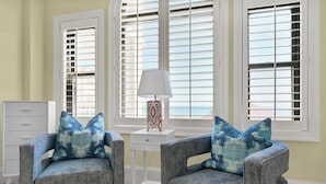 A room with two grey armchairs with blue patterned cushions, a white side table with a lamp, and a white dresser. - 3BR/3BA Dune Ridge Condo with Elevator, Pool & Ocean Views (Wrightsville Beach)