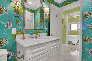 A bathroom with a white vanity, a large mirror, and a floral wallpaper design. - 3BR/3BA Dune Ridge Condo with Elevator, Pool & Ocean Views (Wrightsville Beach)
