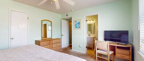 A bedroom with a bed, a desk, a chair, a television, a ceiling fan, and a door.