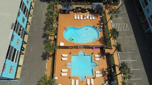 Eine Vogelperspektive eines Hotels mit Swimmingpool, Liegestühlen und Palmen.